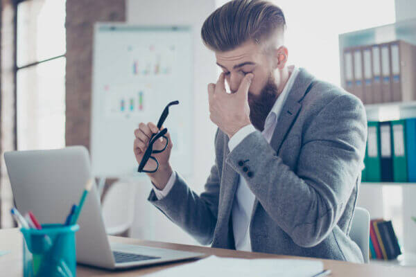 Hipster man in office rubbing his dry eyes
