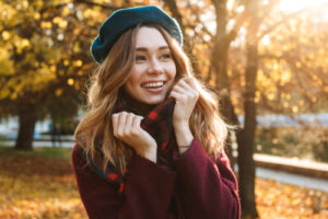 smiling woman in sweater and winter hat with autumn foliage in background
