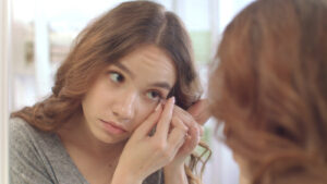 woman looking into mirror as she puts in her contacts 